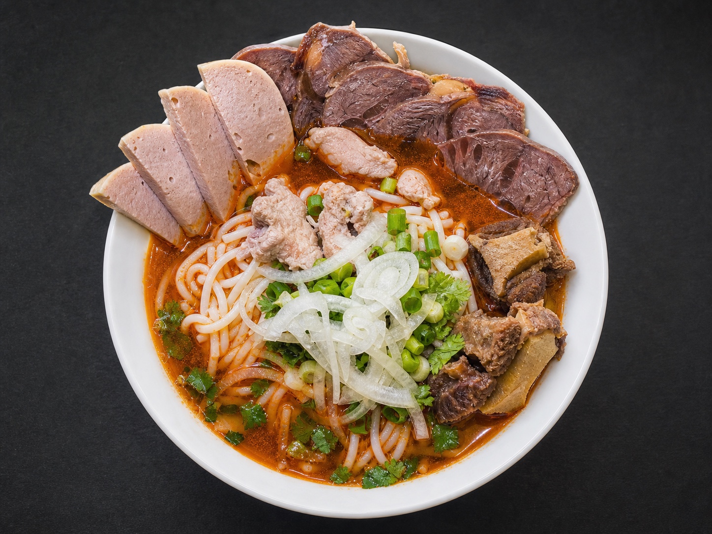 A bowl of bún bò Huế with bone-in beef shank, pork roll, cilantro, and golden broth